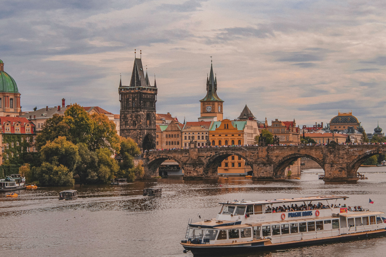 Karlsbrúin í Prag með borgarbyggð og bátum á ánni